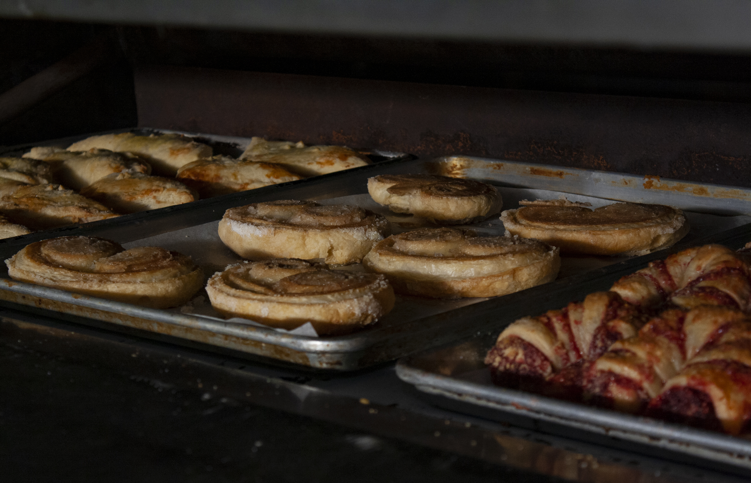 Trays of assorted pastries, including swirled puff pastries, are baking inside an oven.