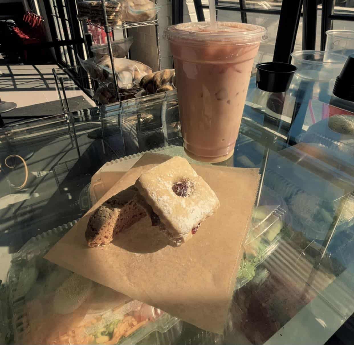 Iced coffee and assorted pastries on a café counter, lit by morning sunlight, creating a warm and inviting coffee shop scene.