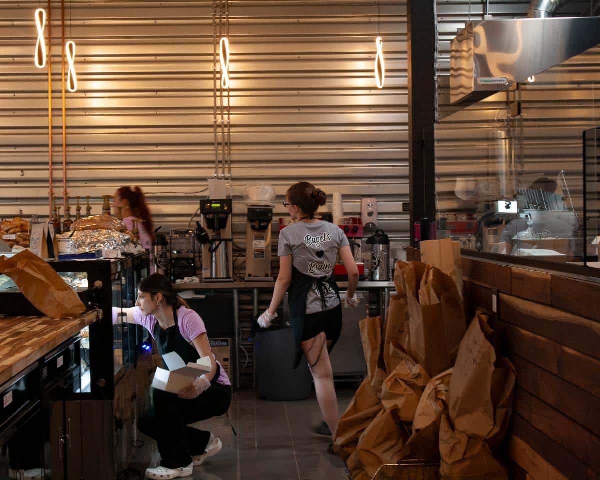 Bagel Chicks staff preparing food behind the counter, highlighting the busy lunchtime rush.