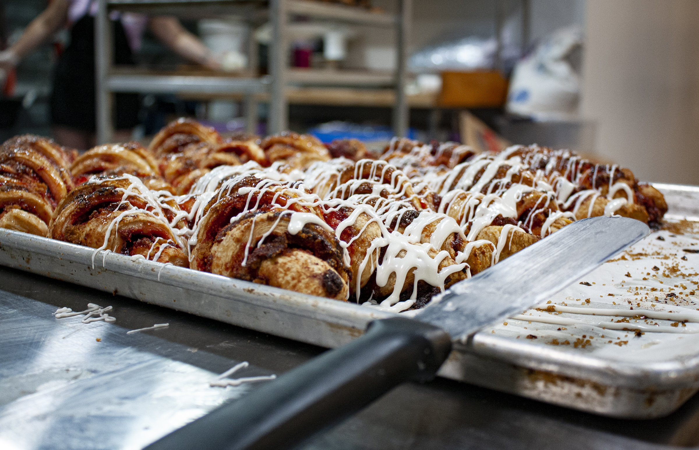 Freshly baked pastries drizzled with icing on a tray in Bagel Chicks’ bakery kitchen, showcasing seasonal fall treats.