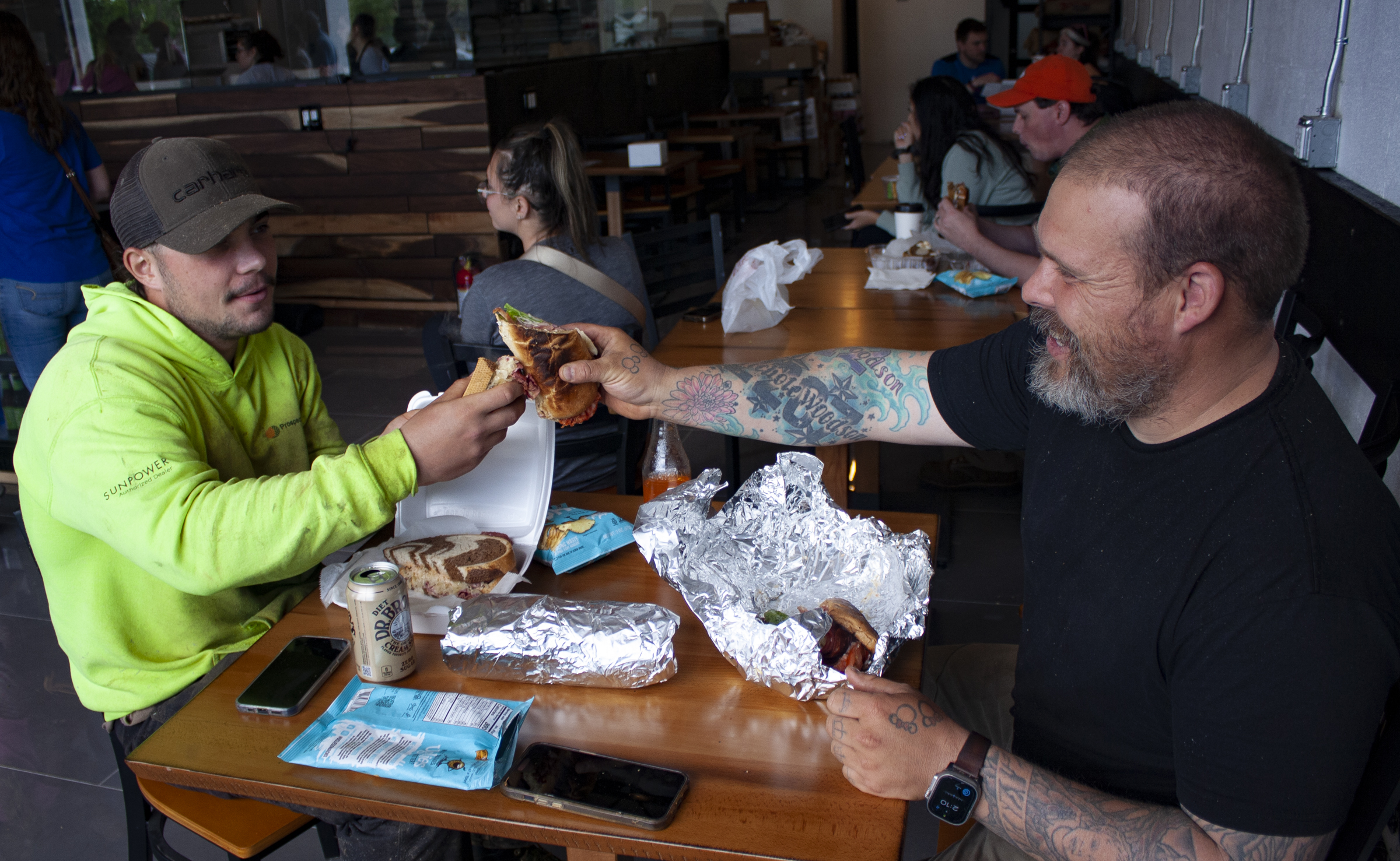 Two men sharing a meal and smiling inside Bagel Chicks Bakery cafรฉ.