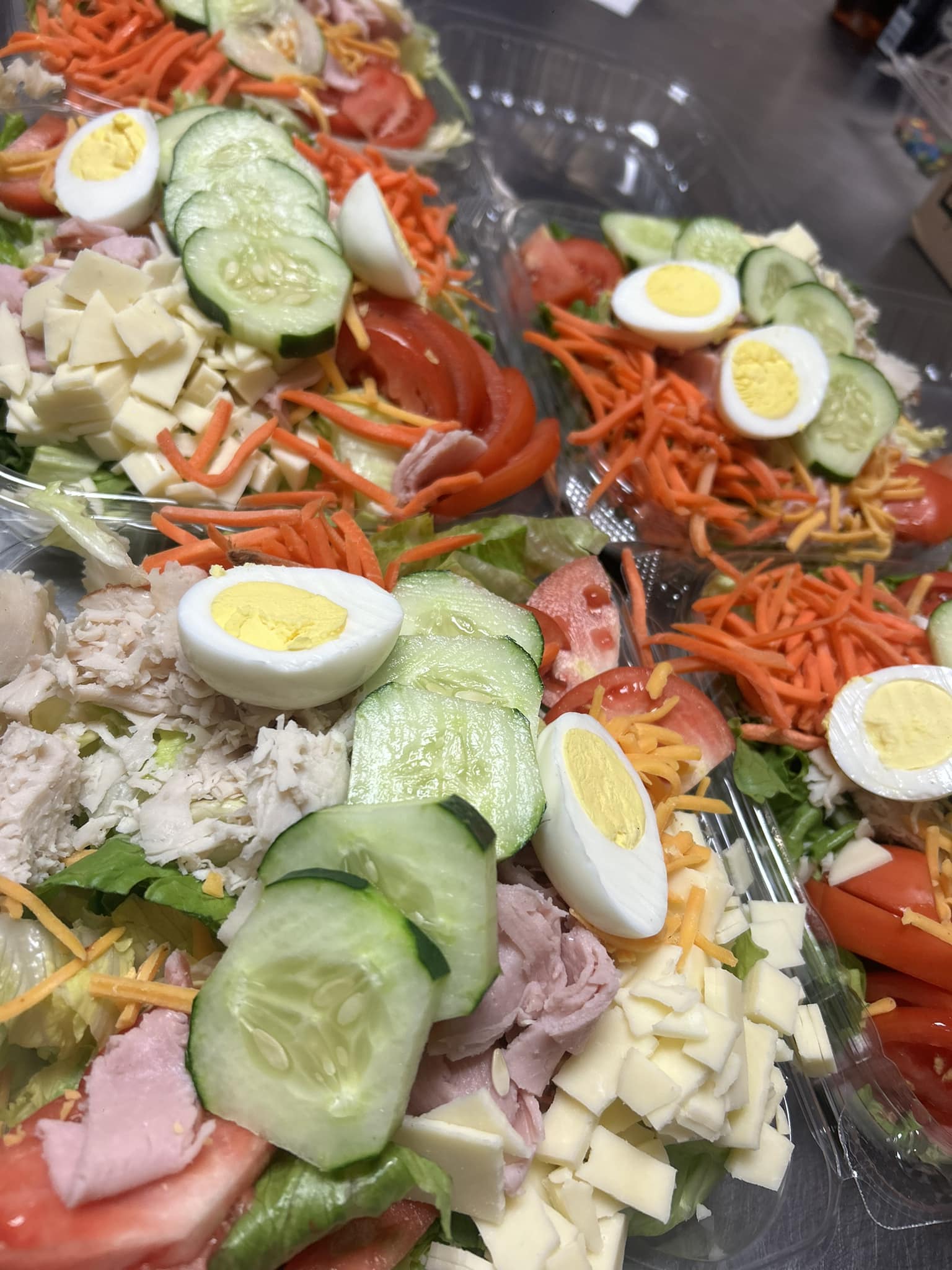 Close-up of chef salads topped with eggs, cucumbers, shredded carrots, ham, turkey, cheese, and tomatoes at Bagel Chicks.