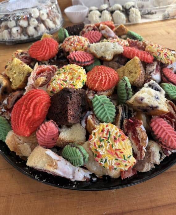 A large tray of assorted cookies, cake pieces, sprinkle pastries, and colorful baked sweets from Bagel Chicks, arranged for a spring picnic or dessert spread.
