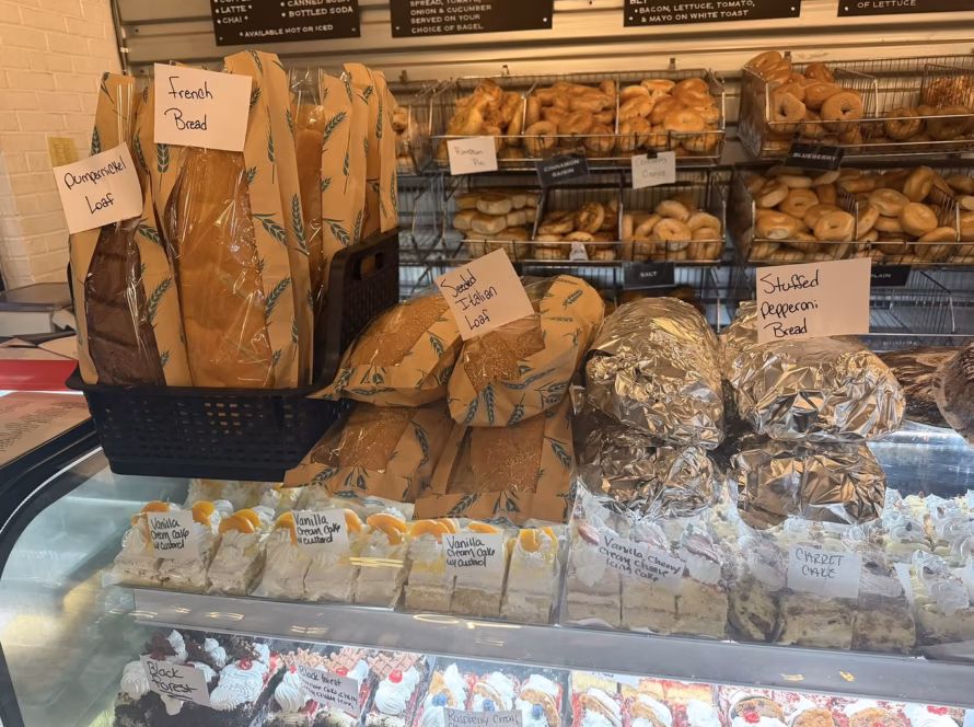 Bakery display with French bread, pumpernickel loaf, seeded Italian bread, stuffed pepperoni bread, bagels, and cakes representing local food culture in West Virginia and Virginia.